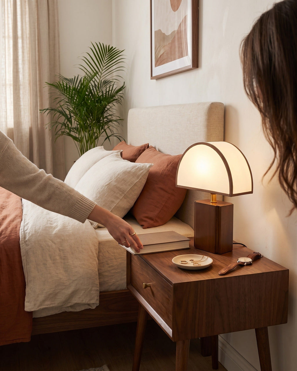 Hand switching on the Halvo half-dome walnut lamp on a bedside table