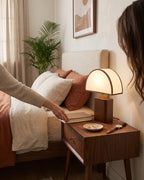 Hand switching on the Halvo half-dome walnut lamp on a bedside table