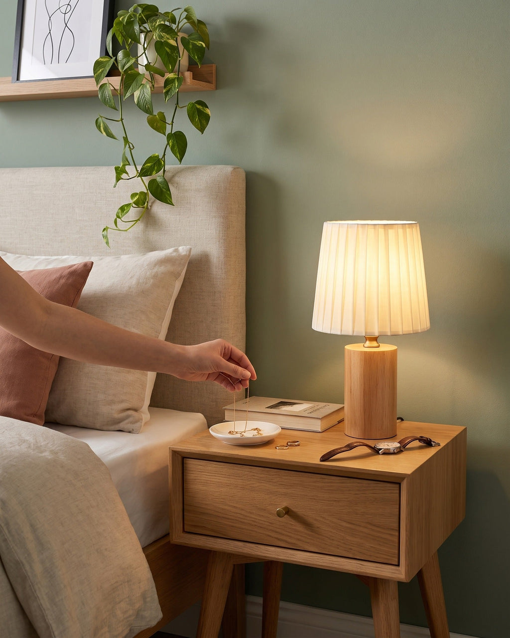Hand placing a book beside the Linnea oak lamp on a bedside table