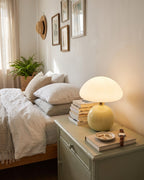 Cream Dolce mushroom lamp on a sage nightstand beside a bed with white linens