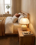 Cream Petal Dome lamp lit on a nightstand beside a bed with rust bedding