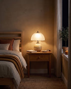 Cream Petal Dome lamp glowing on a wooden nightstand in the evening