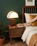 Hand reaching for a book beside the Halvo half-dome lamp on a walnut nightstand