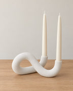 White: Knot Sculptural Double Candle Holder on a light oak tabletop against a seamless studio backdrop