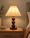 Walnut: Bobbin Trio Wood Nightstand Lamp in walnut lit on a nightstand in the evening