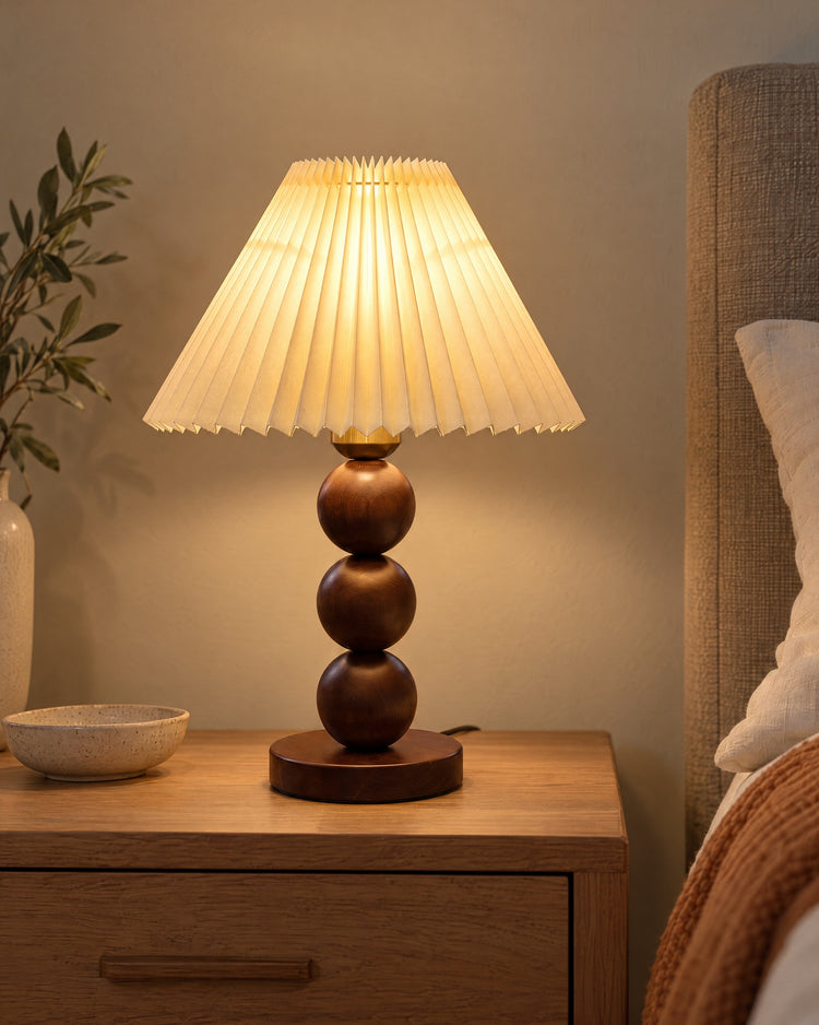Walnut: Bobbin Trio Wood Nightstand Lamp in walnut lit on a nightstand in the evening