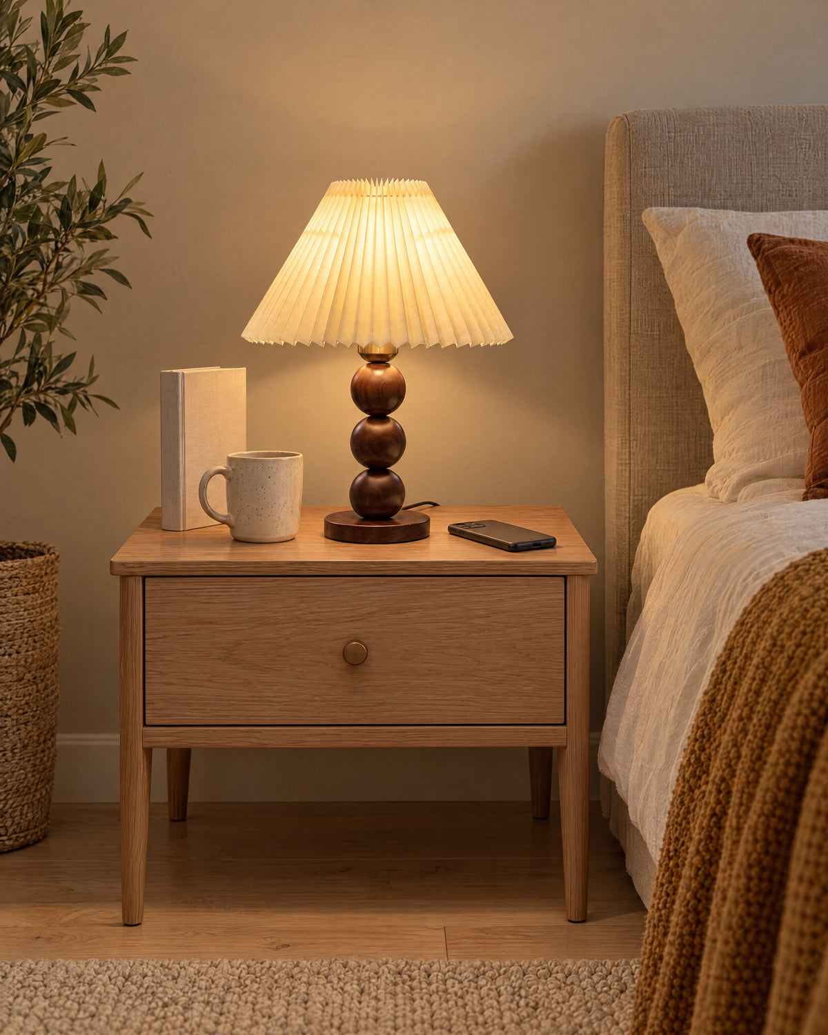 Walnut: Bobbin Trio Wood Nightstand Lamp in walnut on a standard nightstand with a book, phone and mug for scale