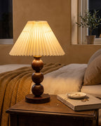 Bobbin Trio walnut lamp with pleated shade on a wood nightstand, warm rustic bedroom