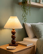 Walnut: Bobbin Trio Wood Nightstand Lamp against a sage green wall with trailing plants