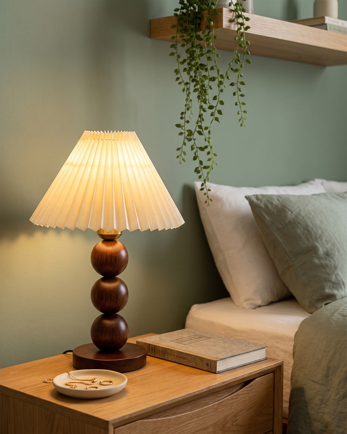 Walnut: Bobbin Trio Wood Nightstand Lamp against a sage green wall with trailing plants