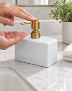 White: A hand pressing the pump of the Ceramic Soap Dispenser, Rectangular, Gold Pump, 13.5 oz