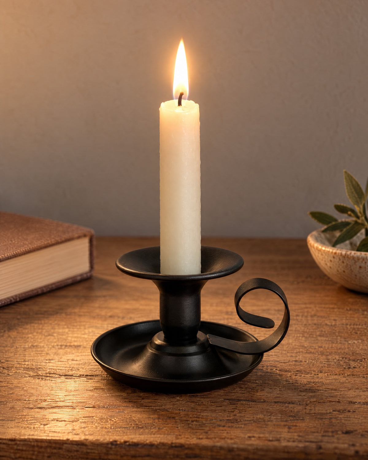 Tazza Iron Teacup Candle Holder, lit, on a styled surface in the evening