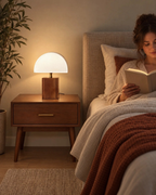 White Trim: Walnut nightstand lamp with a white half dome shade, lit, on a bedside table while a woman reads in bed
