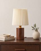 Walnut: Linnea Pleated Wood Nightstand Lamp in walnut on a nightstand top against a plain backdrop