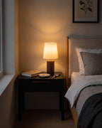 Walnut: Linnea walnut lamp with a pleated shade glowing on a black nightstand at night
