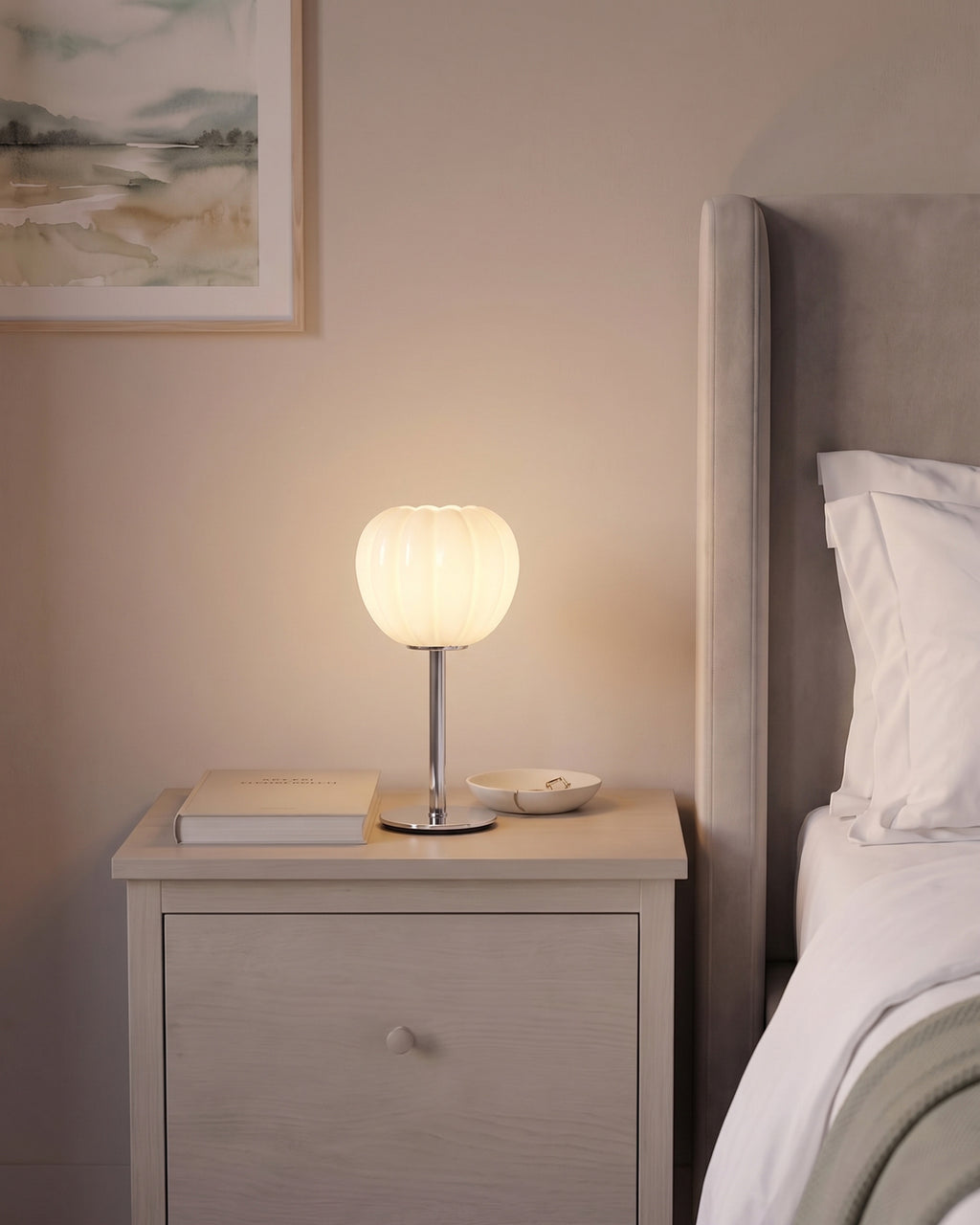Luna Ribbed Opal Glass Nightstand Lamp lit on a pale grey nightstand beside an upholstered bed