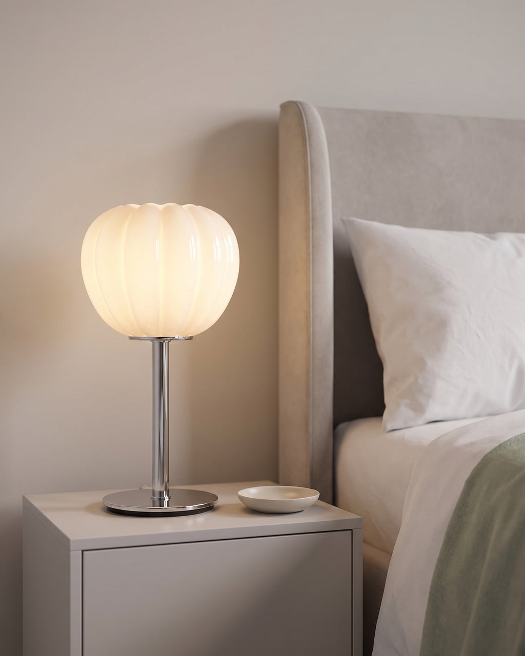 Close-up of the lit Luna Ribbed Opal Glass Nightstand Lamp on a nightstand beside a greige upholstered headboard
