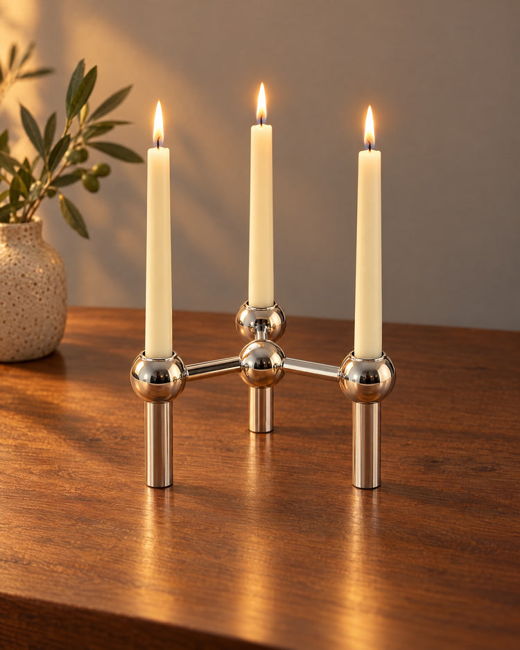 Silver: Orbit Stackable Metal Candlestick, lit, on a styled surface in the evening