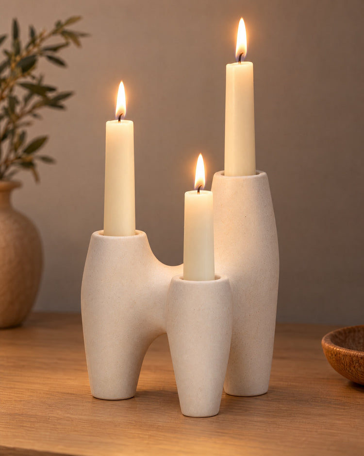 Duna Sculptural Ceramic Candle Holder, lit, on a styled surface in the evening