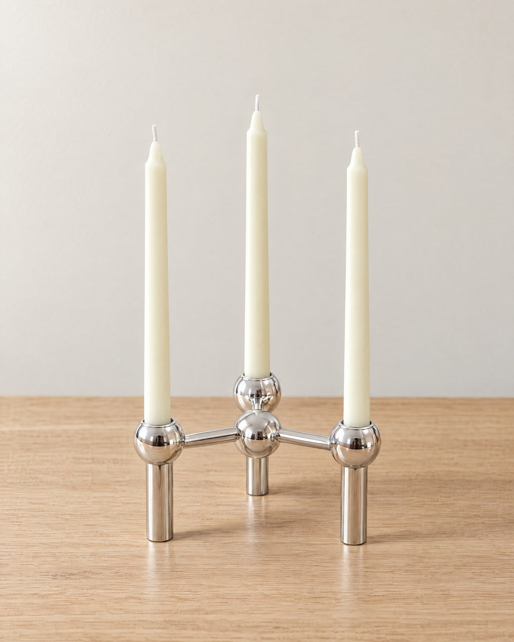 Silver: Orbit Stackable Metal Candlestick on a light oak tabletop against a seamless studio backdrop