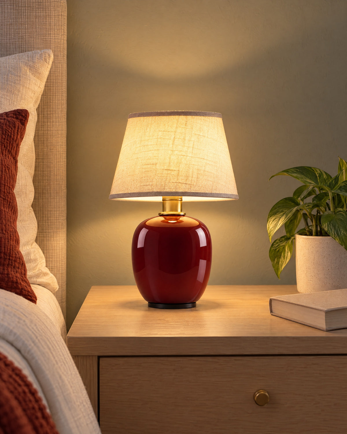 Burgundy: Vessel Cordless Ceramic Nightstand Lamp switched on on a nightstand in the evening