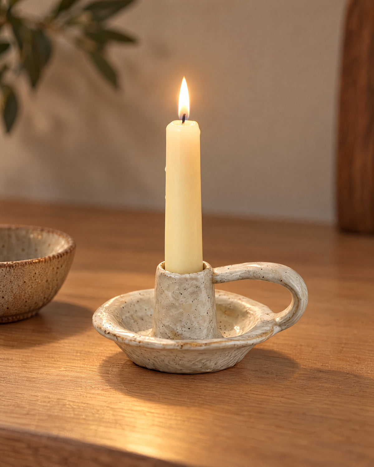 Wabi Speckled Ceramic Chamberstick, lit, on a styled surface in the evening