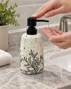 A hand pressing the pump of the White Soap Dispenser, Speckled Ceramic, Black Pump, 11 oz